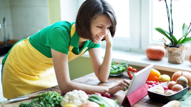 Woman reading a recipe at a kitchen counter full of fruits and vegetables